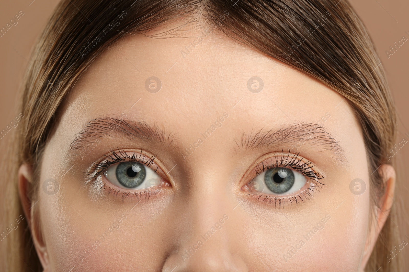 Photo of Woman with long eyelashes after mascara applying against light brown background, closeup
