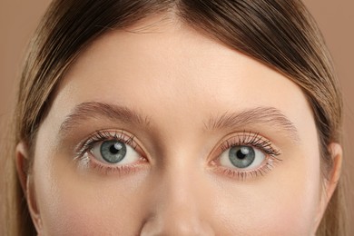 Woman with long eyelashes after mascara applying against light brown background, closeup