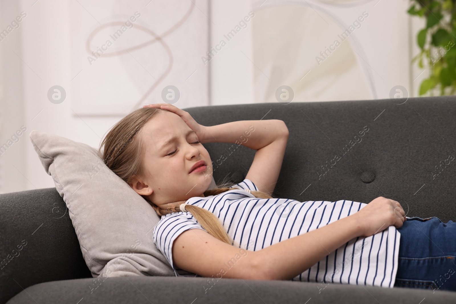 Photo of Little girl suffering from headache on sofa indoors