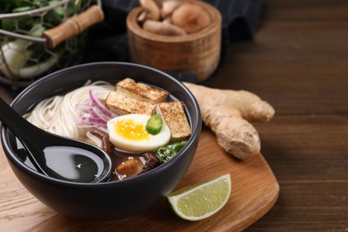 Photo of Delicious vegetarian ramen in bowl and products on wooden table, closeup. Space for text