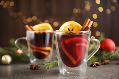 Photo of Glass cups with mulled wine on grey table against festive lights