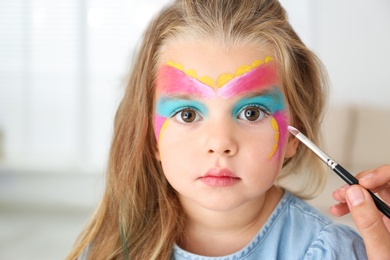 Artist painting face of little girl indoors
