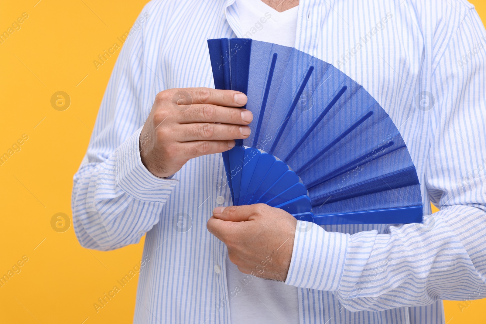 Photo of Man holding hand fan on orange background, closeup