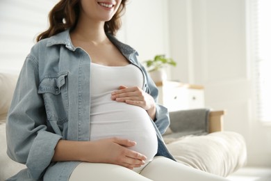 Photo of Pregnant woman touching her belly indoors, closeup