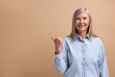 Portrait of beautiful middle aged woman pointing at something on beige background, space for text