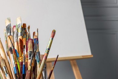 Easel with blank canvas and different art supplies near grey wall, closeup. Space for text