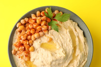 Photo of Bowl of tasty hummus with chickpeas and parsley on yellow background, top view