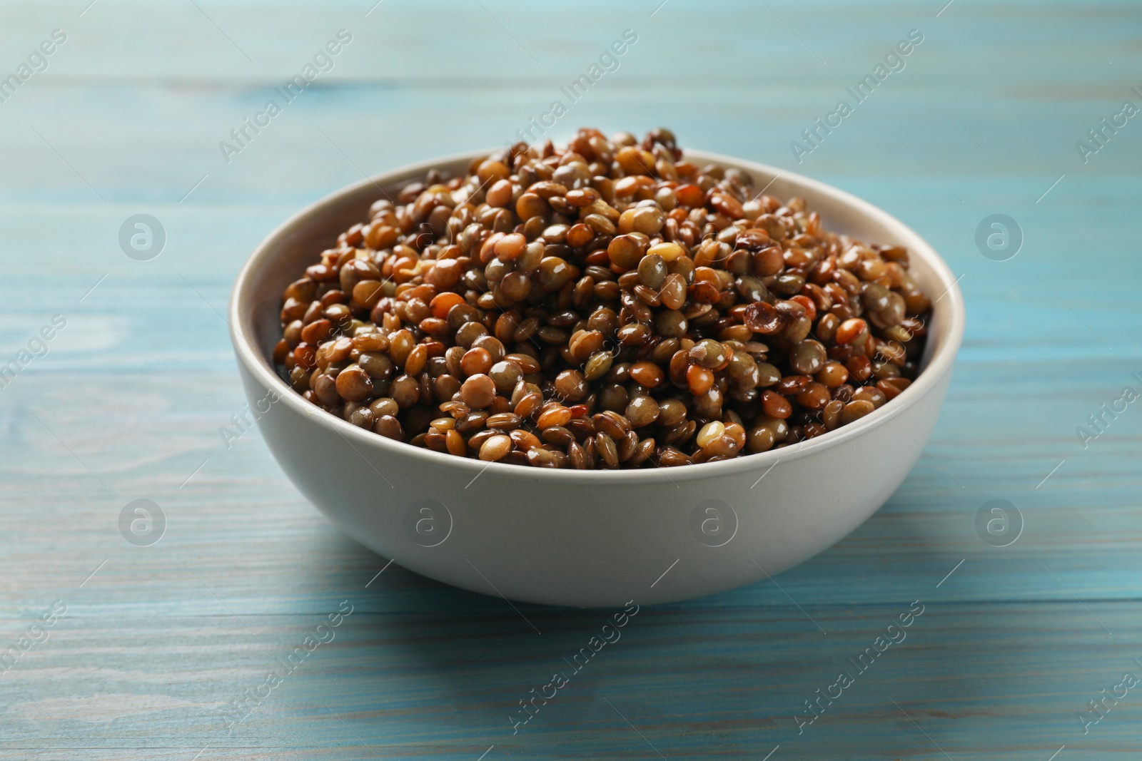 Photo of Delicious lentils in bowl on light blue wooden table, closeup