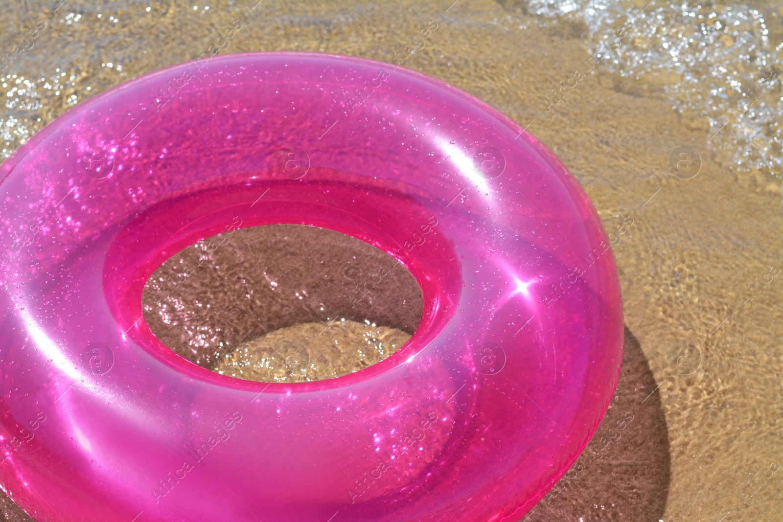 Photo of Bright inflatable ring on sandy beach near sea, closeup