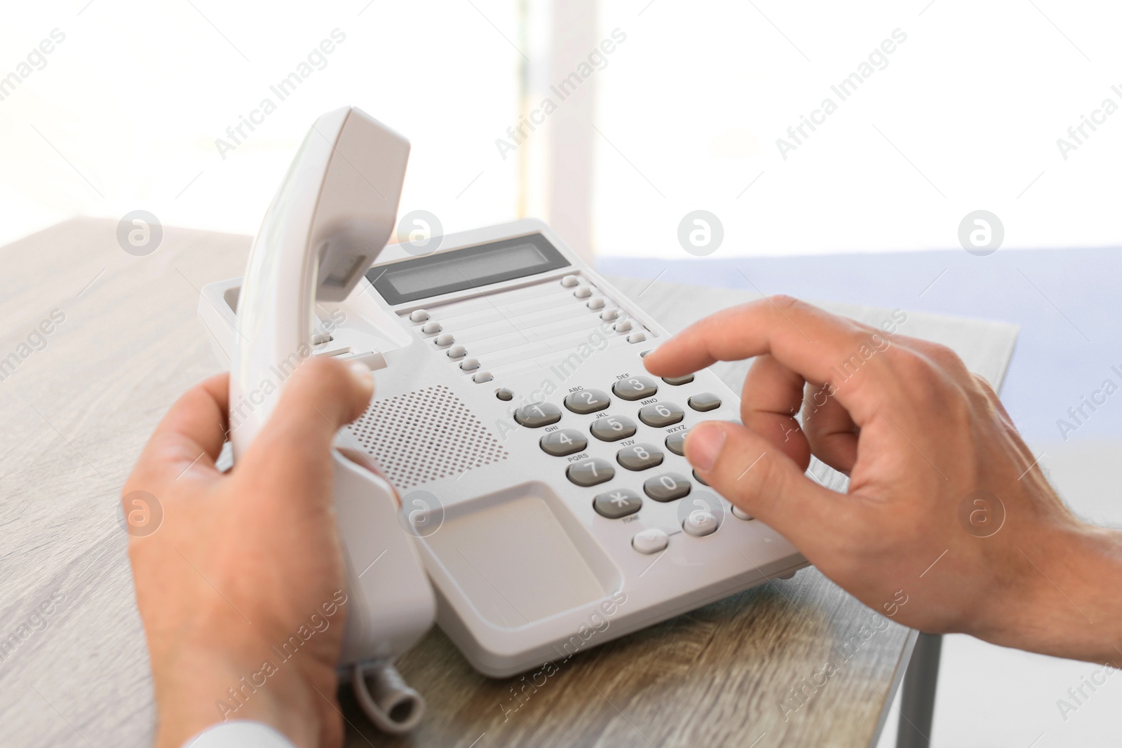 Photo of Man dialing number on telephone at table indoors