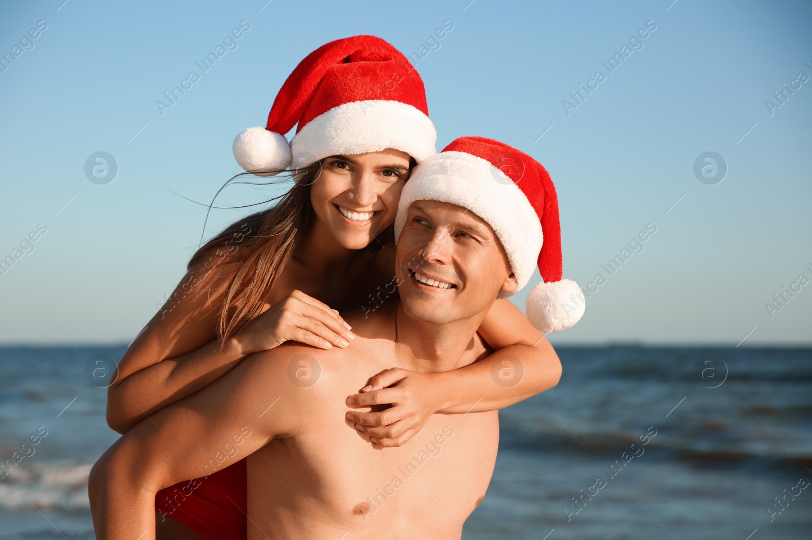 Photo of Happy couple with Santa hats together on beach. Christmas vacation