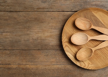 Plate and spoons on wooden table, top view with space for text. Cooking utensils