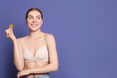Woman in bra holding condom on purple background, space for text. Safe sex