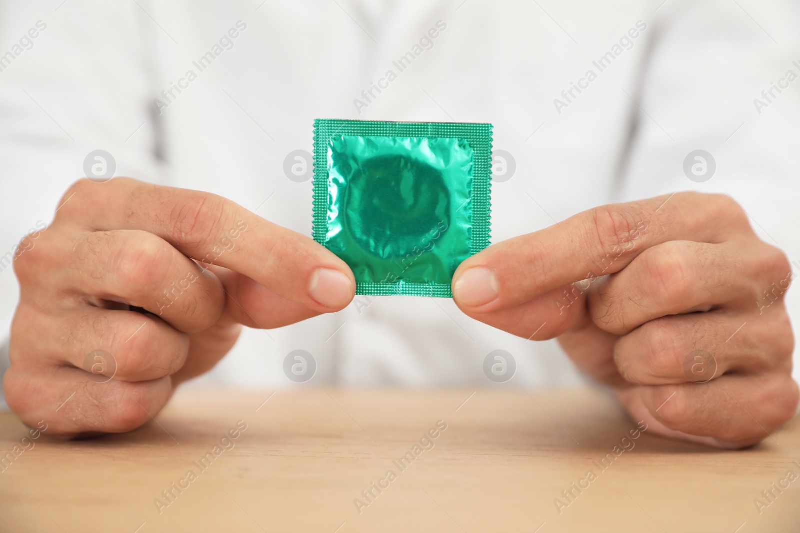 Photo of Doctor holding condom at wooden table, closeup. Safe sex concept