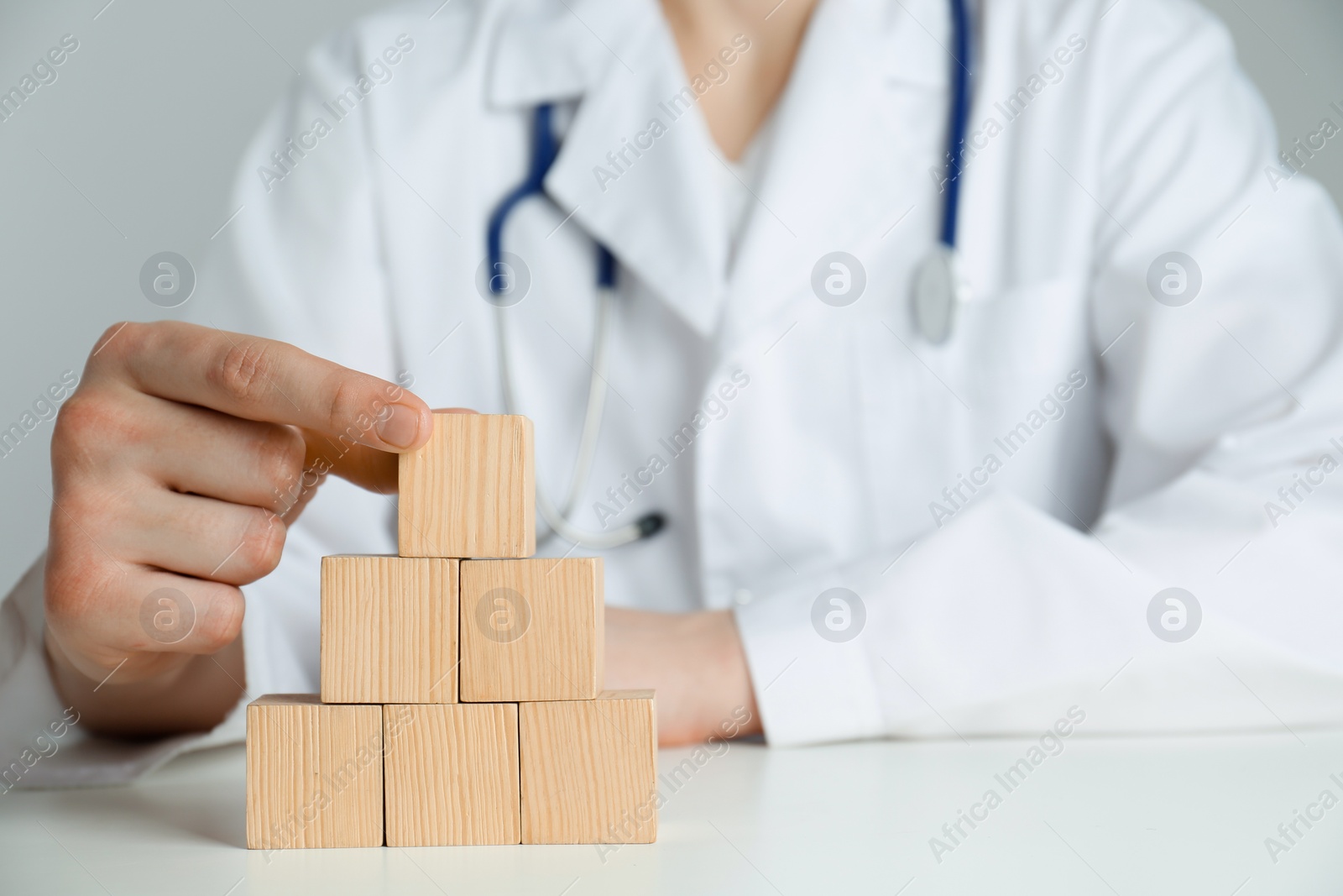 Photo of Doctor building pyramid of blank wooden cubes on white table against light background, closeup. Space for text