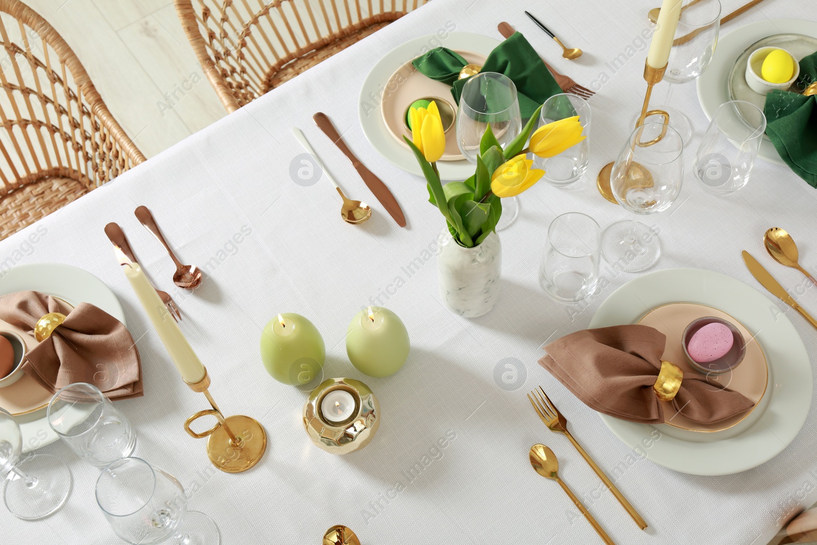 Photo of Festive Easter table setting with painted eggs, burning candles and yellow tulips indoors, view from above