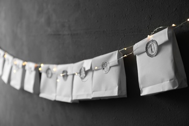 Photo of Paper bags hanging on black wall, closeup. Christmas advent calendar