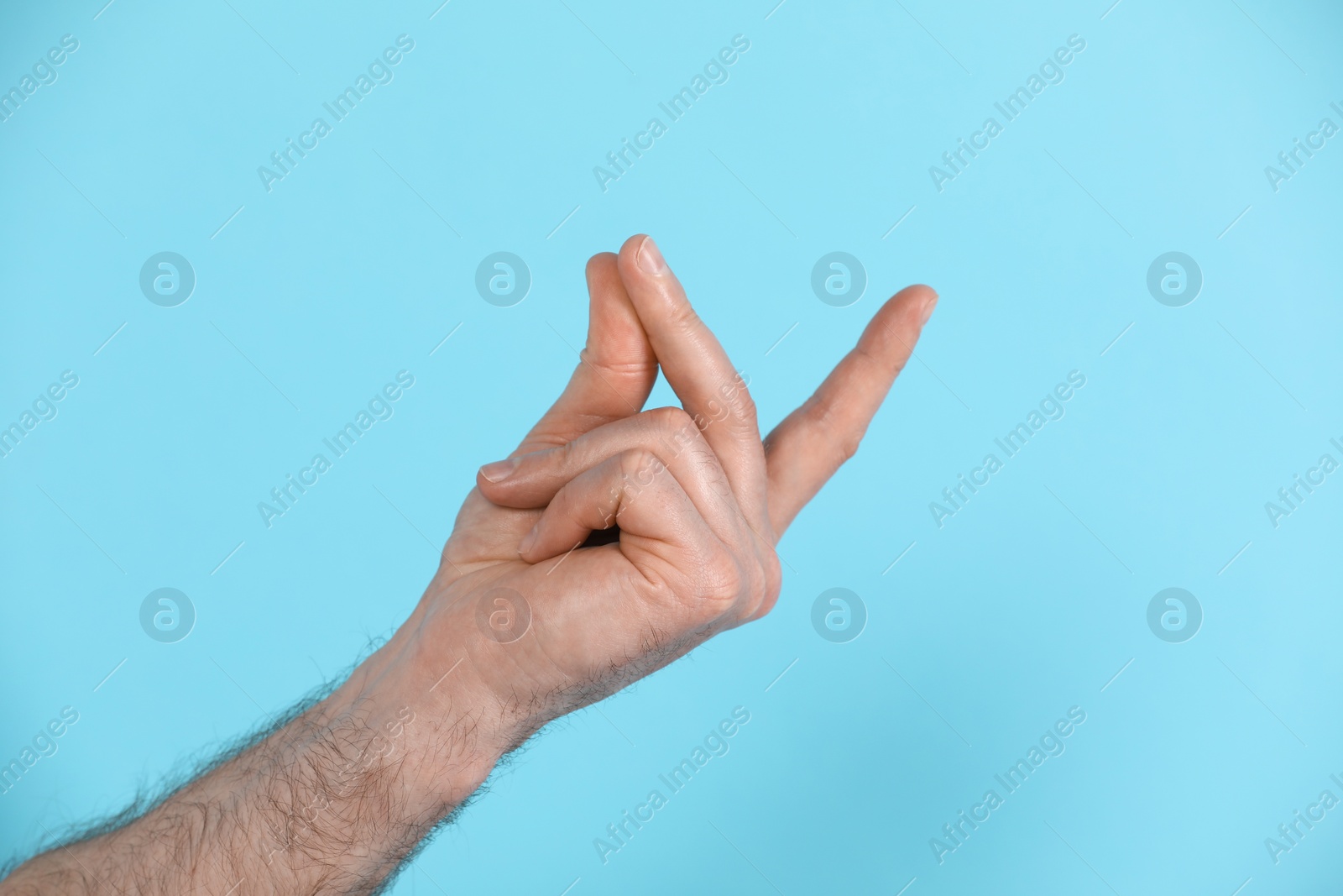 Photo of Man snapping his fingers on light blue background, closeup. Bad habit