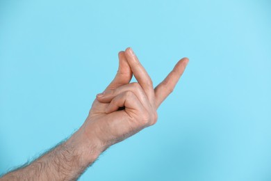Man snapping his fingers on light blue background, closeup. Bad habit
