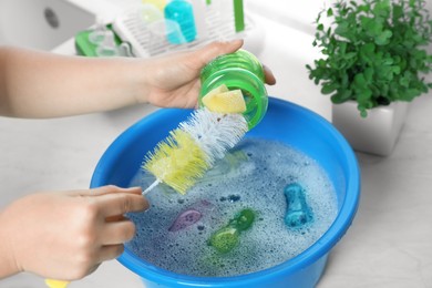 Photo of Woman washing baby bottle above basin in kitchen, closeup