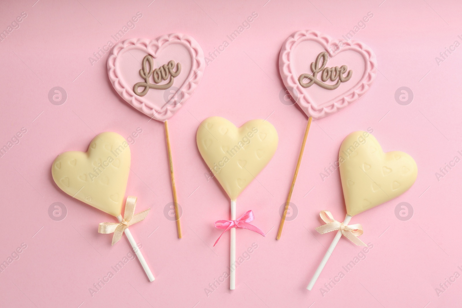 Photo of Different chocolate heart shaped lollipops on light pink background, flat lay