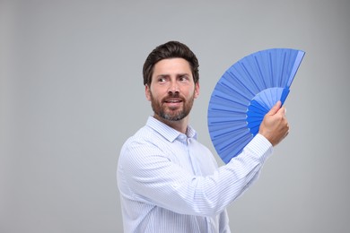 Happy man holding hand fan on light grey background