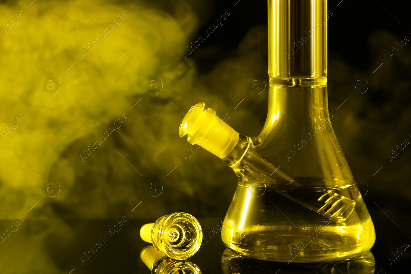 Photo of Closeup view of glass bong with smoke on black background, toned in yellow. Smoking device
