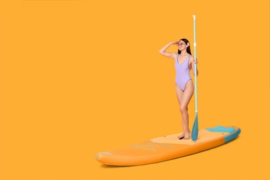 Photo of Happy woman with paddle on SUP board against orange background, space for text
