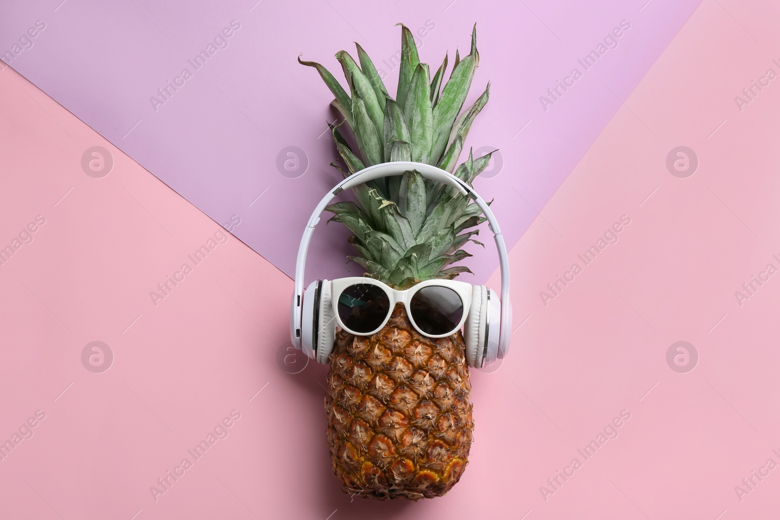 Photo of Pineapple with headphones and sunglasses on color background, top view. Creative concept