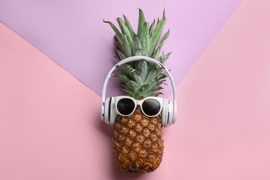 Photo of Pineapple with headphones and sunglasses on color background, top view. Creative concept