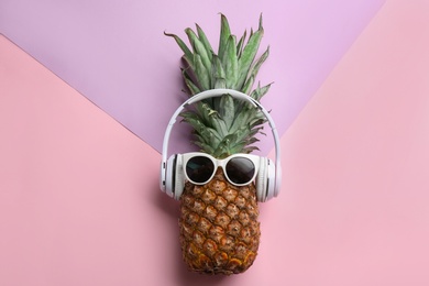 Pineapple with headphones and sunglasses on color background, top view. Creative concept