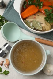 Hot delicious bouillon and ingredients on light grey table, flat lay