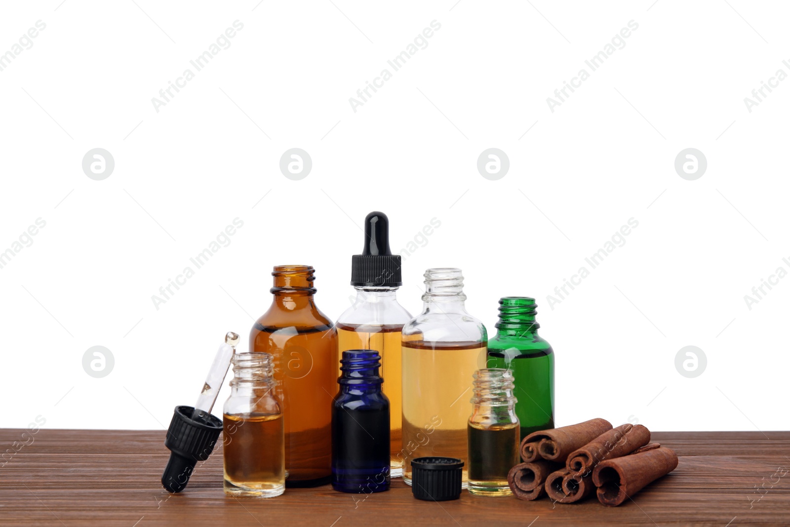 Photo of Bottles of essential oils and cinnamon sticks on wooden table against white background