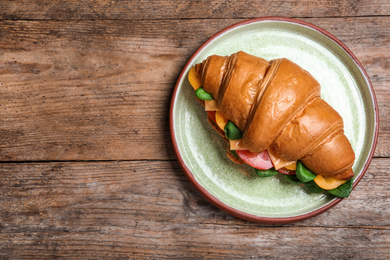 Photo of Tasty croissant sandwich on wooden table, top view. Space for text