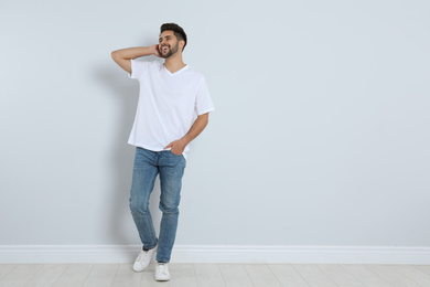 Photo of Young man in stylish jeans near light wall. Space for text