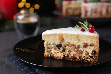 Photo of Slice of traditional Christmas cake decorated with rosemary and cranberries on black table, closeup