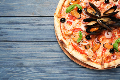 Photo of Tasty pizza with seafood and fresh basil on blue wooden table, top view. Space for text