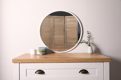 Photo of Trendy round mirror and chest of drawers near white wall. Interior element