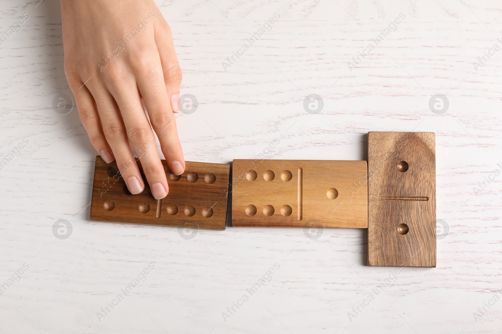 Photo of Woman playing dominoes at white table, top view