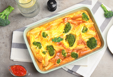 Tasty broccoli casserole in baking dish on grey table, flat lay