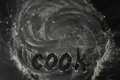 Photo of White flour and word COOK on black table, top view. Space for text
