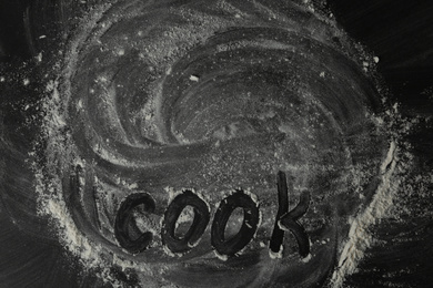 White flour and word COOK on black table, top view. Space for text