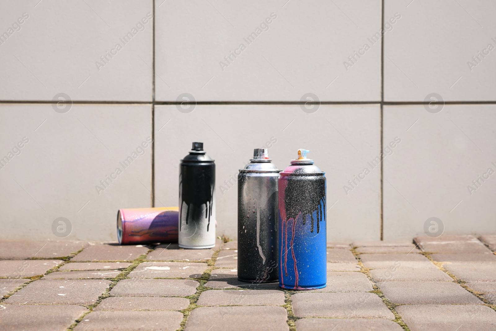 Photo of Used cans of spray paint on pavement near white tile wall outdoors, space for text. Graffiti supplies