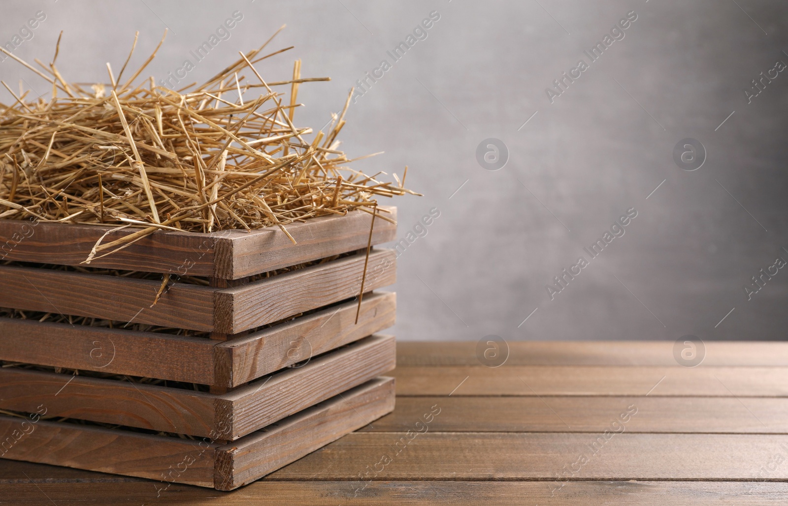 Photo of Dried straw in crate on wooden table, space for text