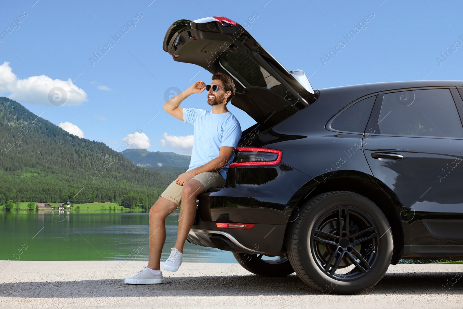 Image of Happy man sitting in trunk of modern car in mountains