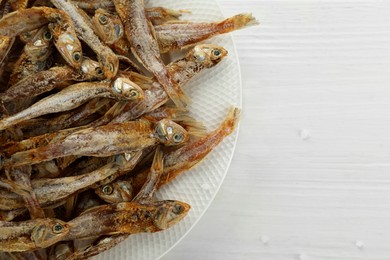 Photo of Plate with tasty dried anchovies on white wooden table, top view. Space for text