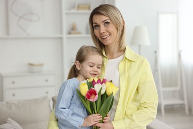 Little daughter congratulating her mom with bouquet of tulips at home. Happy Mother's Day