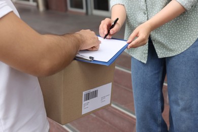 Photo of Woman signing for delivered parcel outdoors, closeup