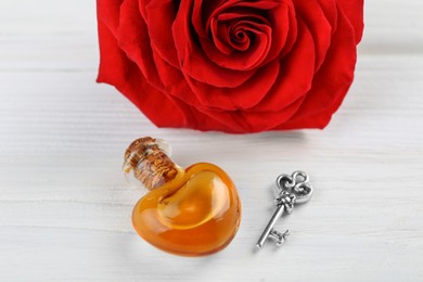 Photo of Heart shaped bottle of love potion with small key and red rose on white wooden table