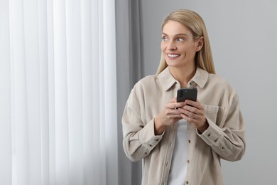 Happy woman sending message via smartphone at home, space for text